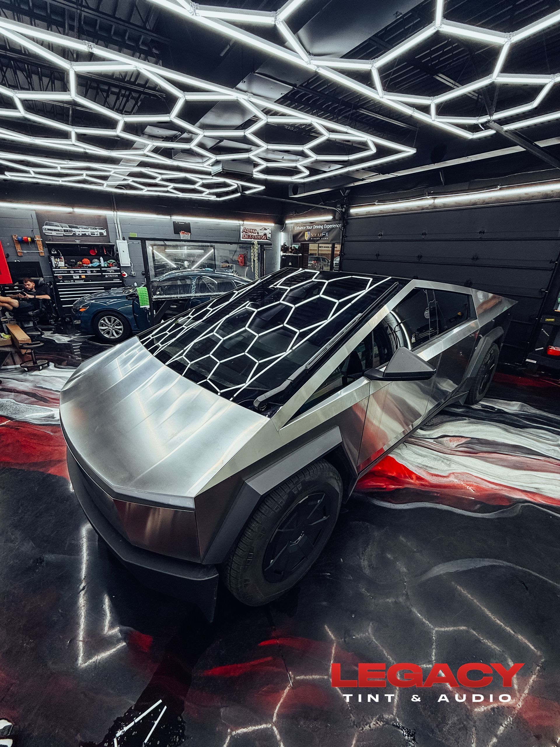 Futuristic silver concept car in a neon-lit showroom with geometric ceiling lights.