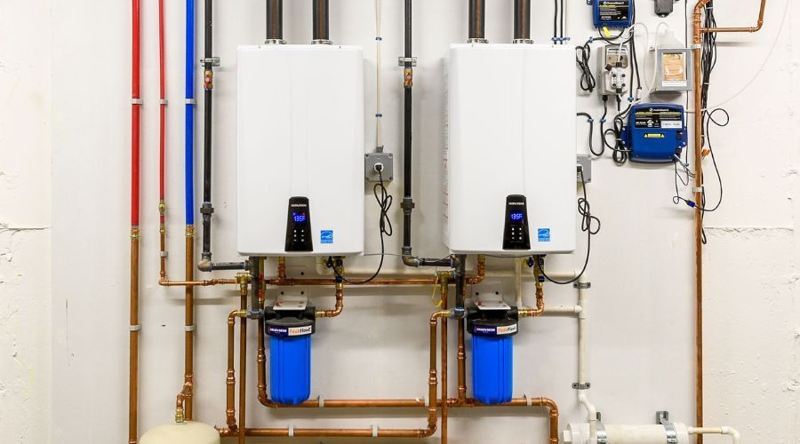 Two white tankless water heaters on a wall, copper pipes, blue water filters.