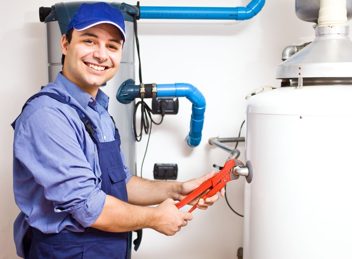 Smiling plumber in blue uniform working on a water heater, inside a utility room.