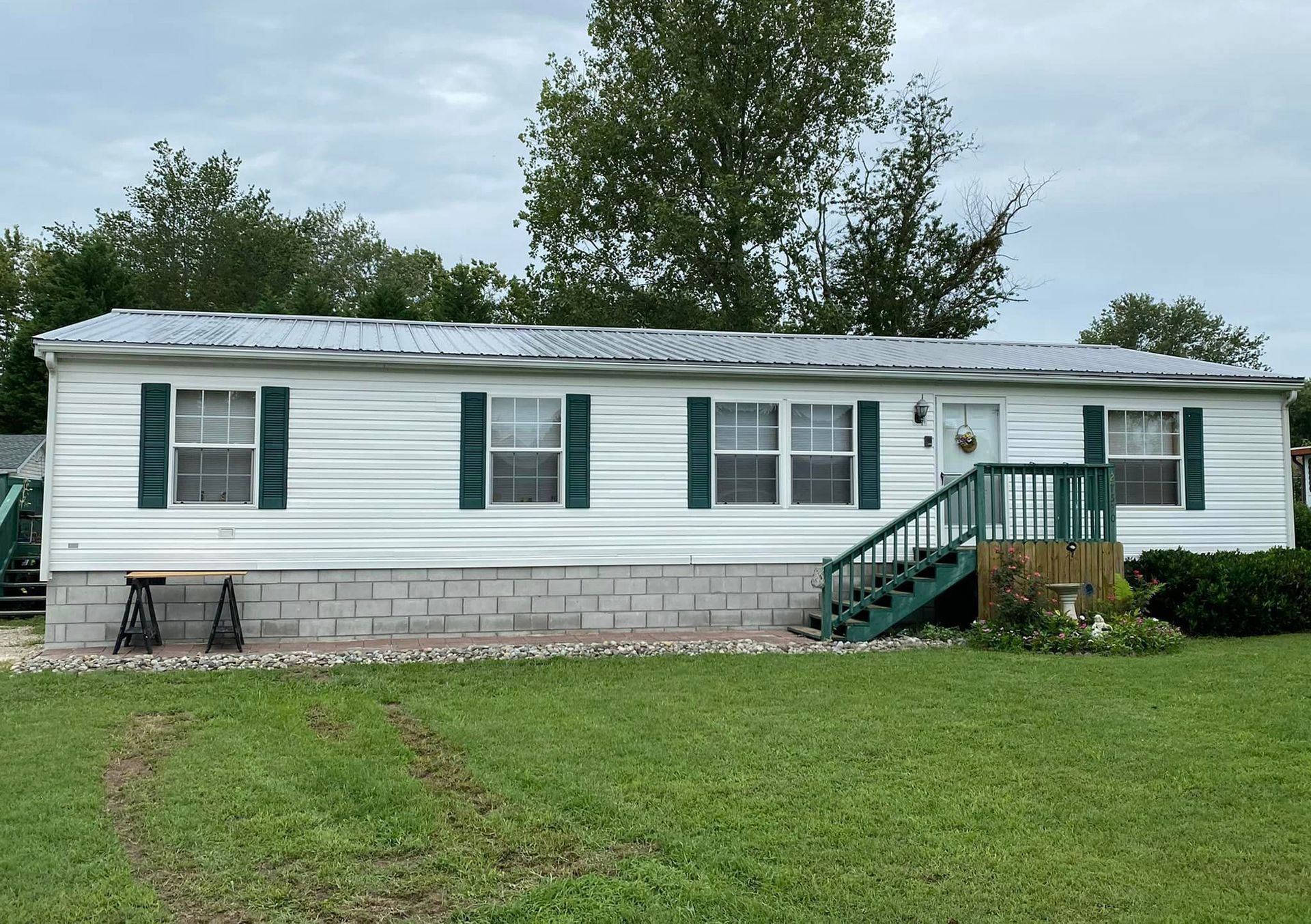 A white mobile home with green shutters and stairs.