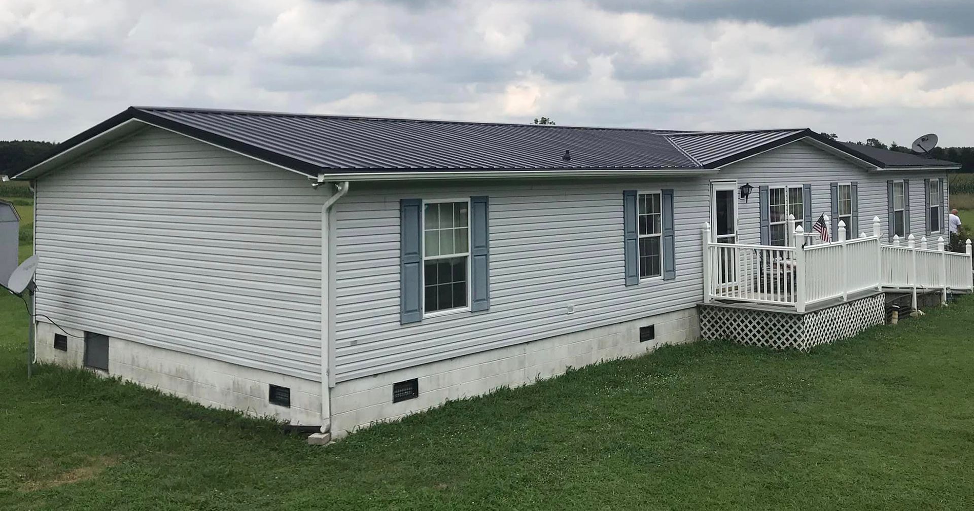 A white mobile home with a black roof is sitting on top of a lush green field.