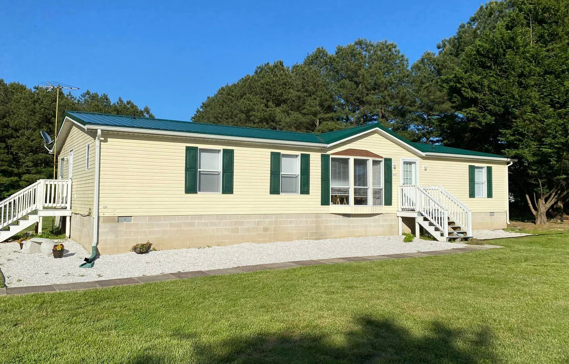 A mobile home with a green roof is sitting in the middle of a grassy field.