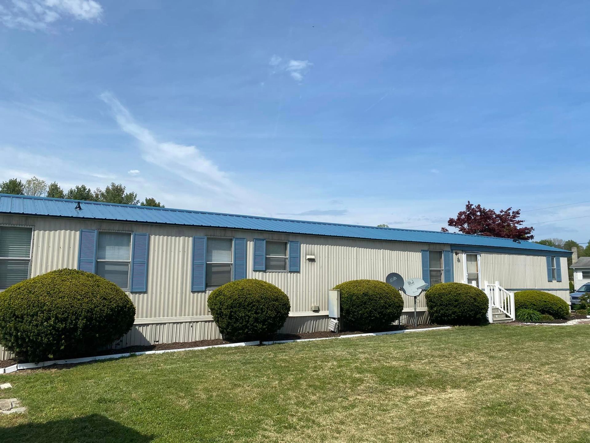 A mobile home with a blue roof is sitting on top of a lush green field.