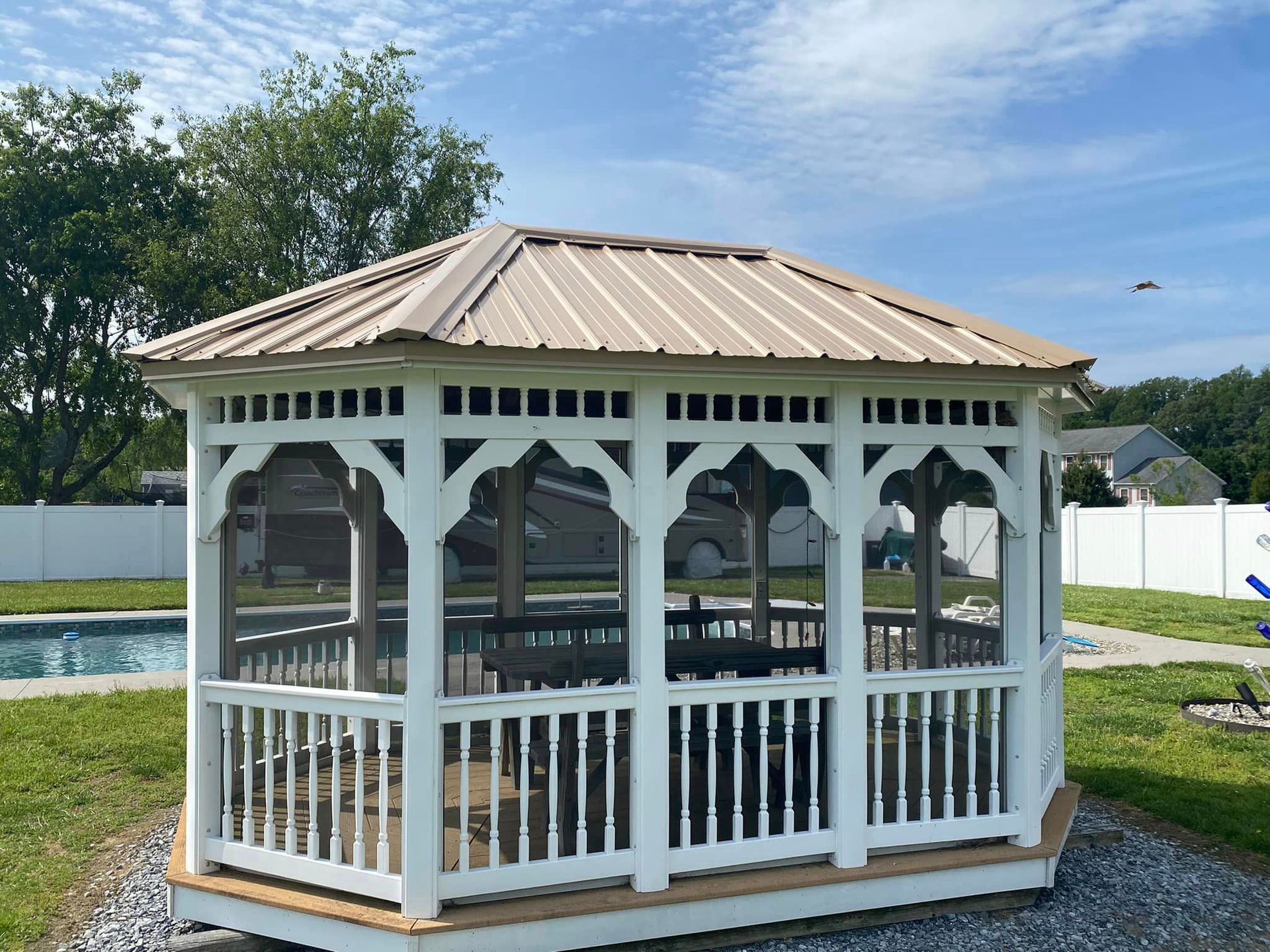 A white gazebo with a brown roof is sitting next to a pool.