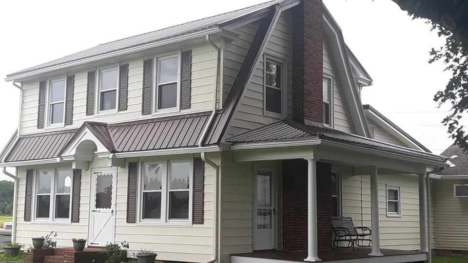 A large white house with a brown roof and a porch.