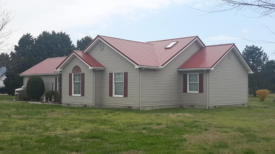 A house with a red roof is sitting in the middle of a grassy field.