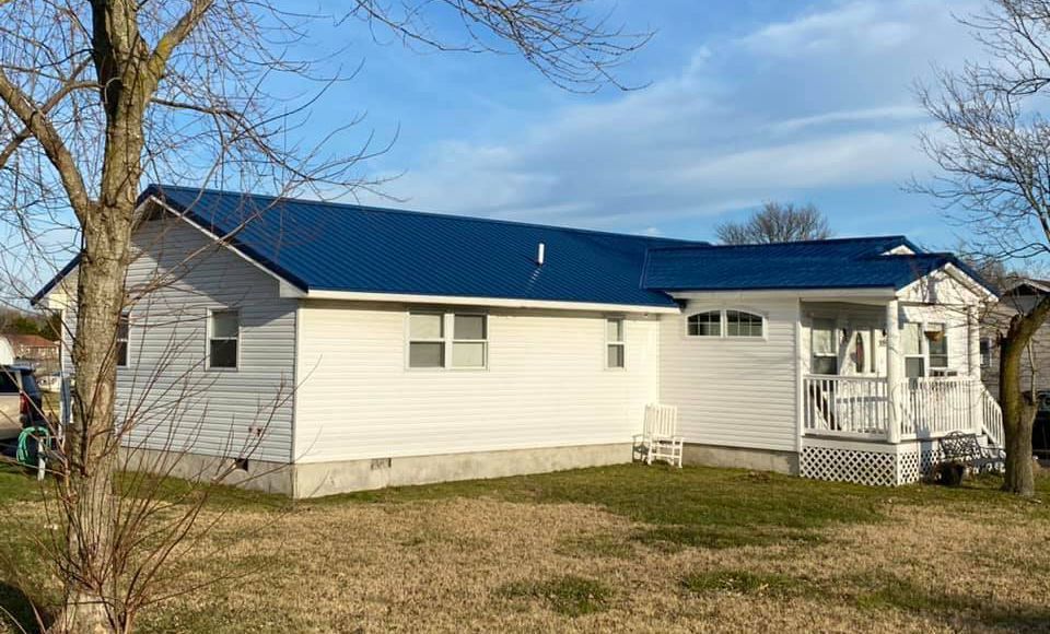 A white house with a blue roof and a tree in front of it.