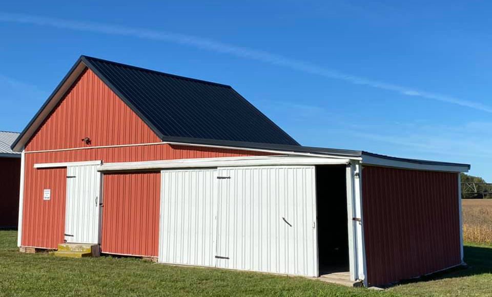 A red and white barn with a black roof is sitting in the middle of a grassy field.