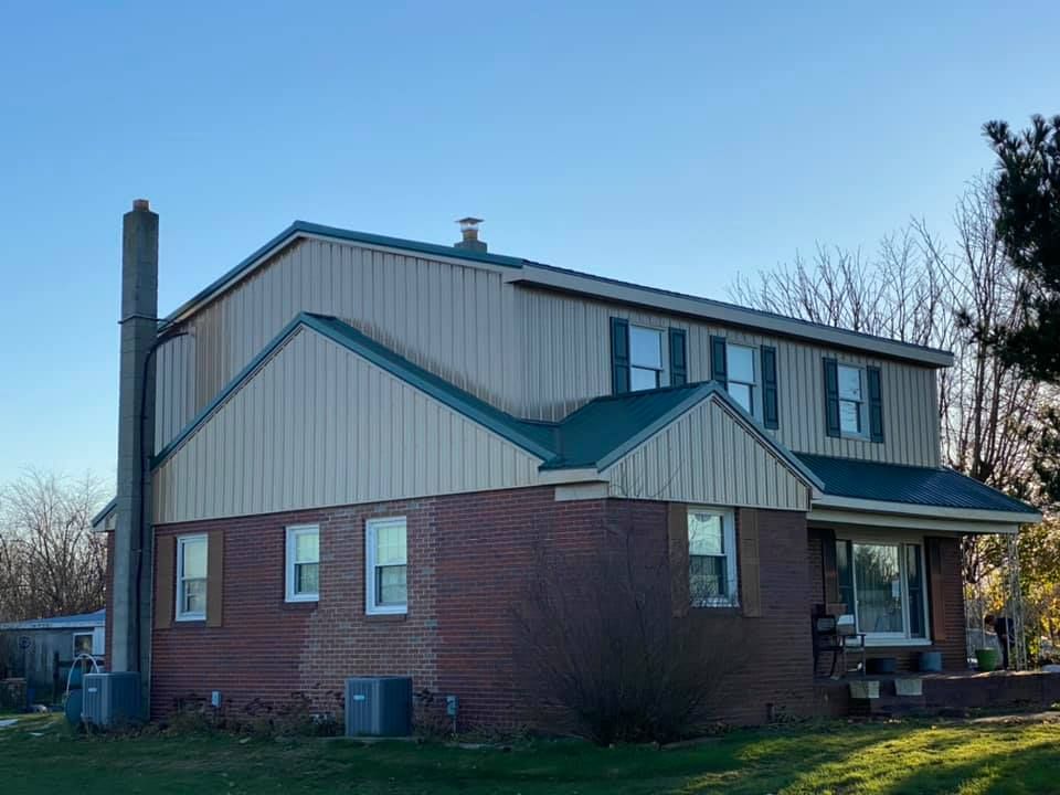 A brick house with a metal siding and a green roof.