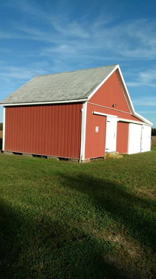 A red barn with white trim is sitting in the middle of a grassy field.