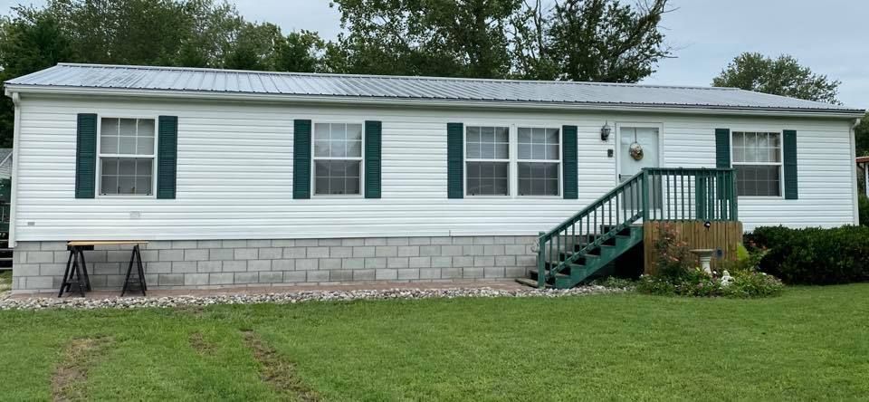 A white mobile home with green shutters and stairs.