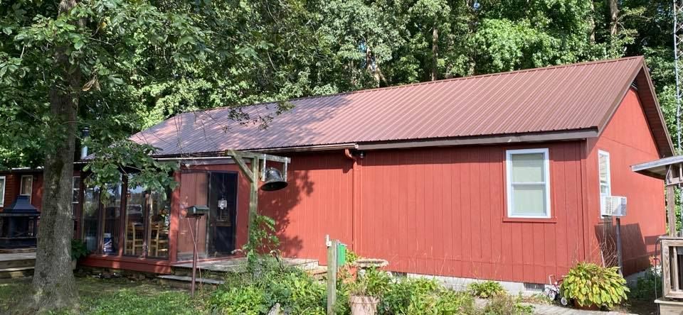 A small red house with a metal roof is surrounded by trees.
