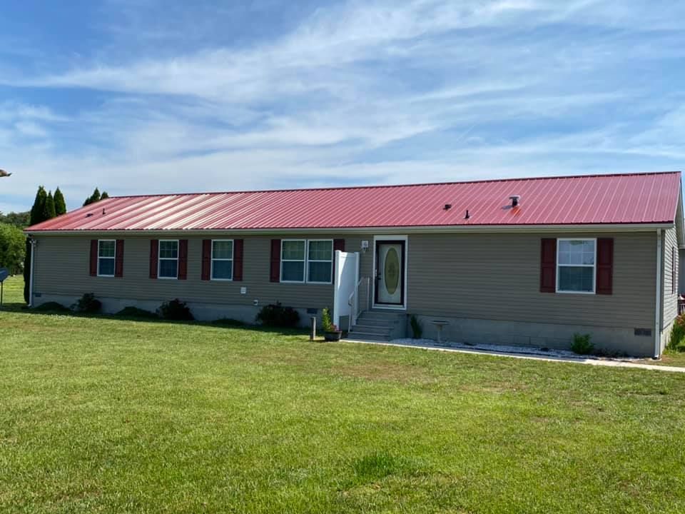 A mobile home with a red roof is sitting on top of a lush green field.