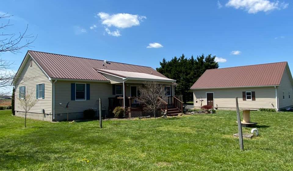 A house with a red roof is sitting on top of a lush green field.