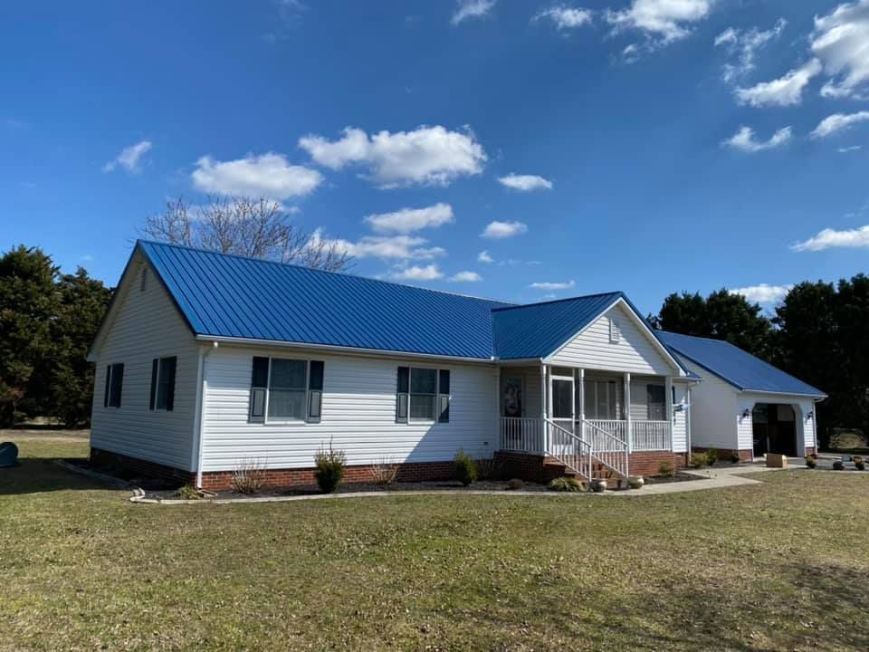 A white house with a blue roof is sitting on top of a lush green field.
