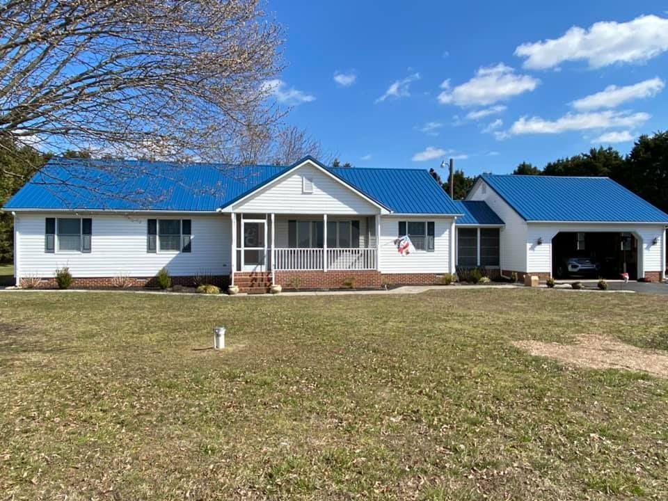 A white house with a blue roof is sitting on top of a lush green field.