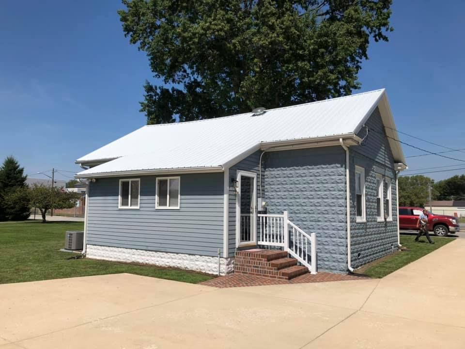 A small blue house with a white roof and a red truck parked in front of it.