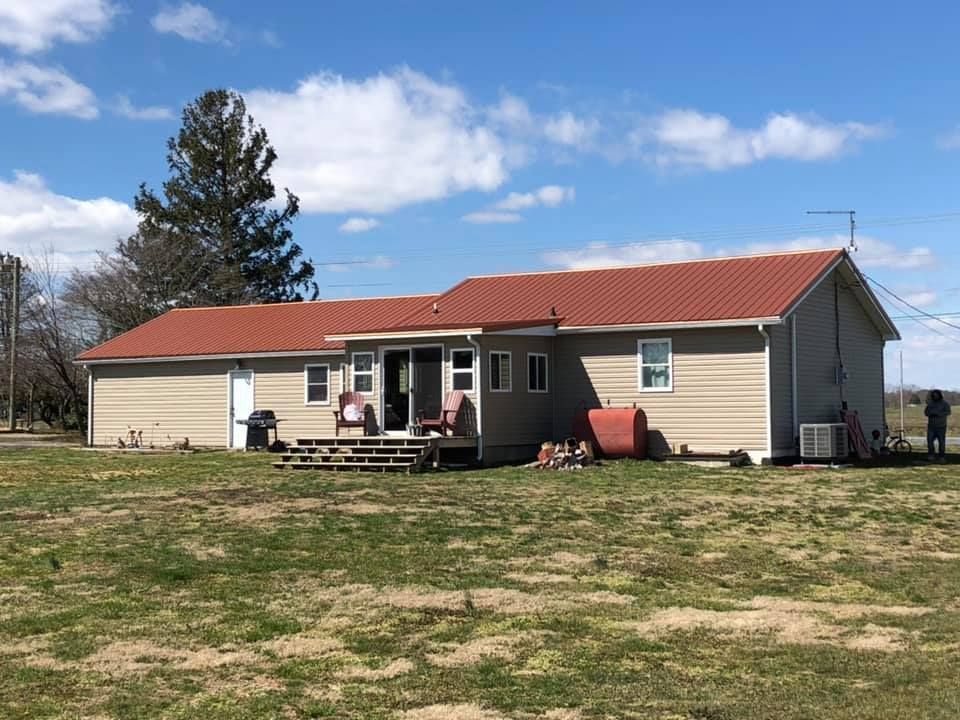 A house with a red roof is sitting in the middle of a grassy field.