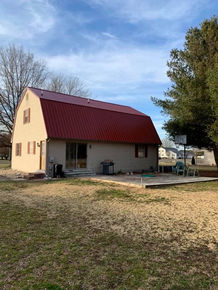 A barn with a red roof is sitting in the middle of a grassy field.