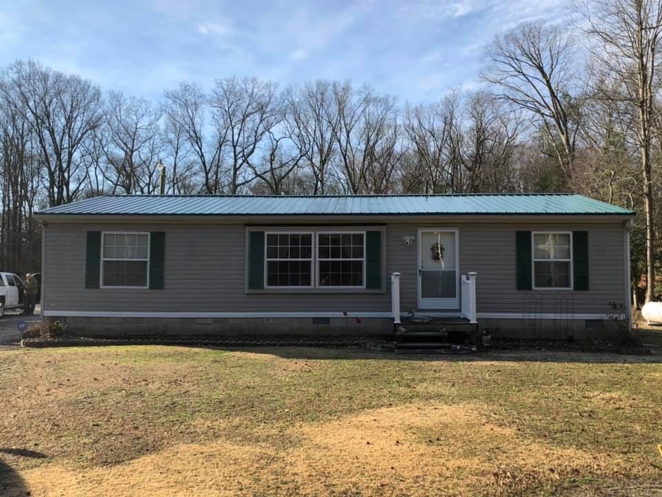 A mobile home with a metal roof and green shutters is sitting in the middle of a grassy field.