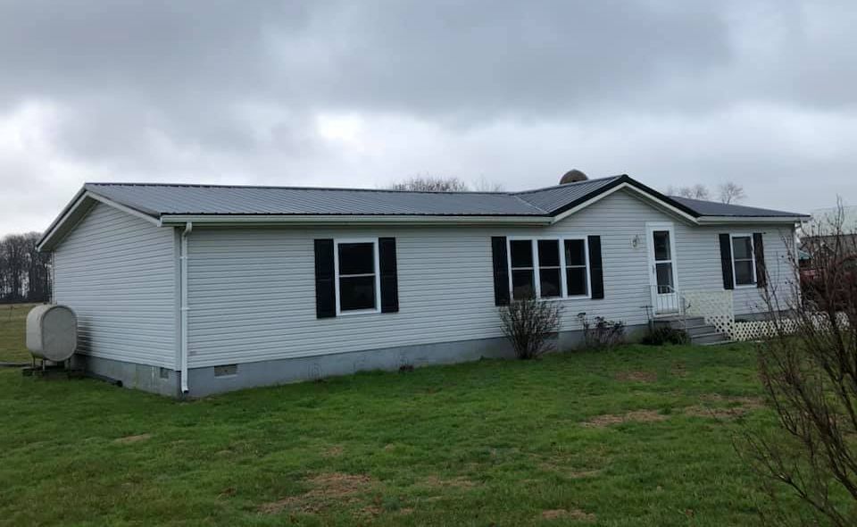 A white mobile home with black shutters is sitting on top of a lush green field.