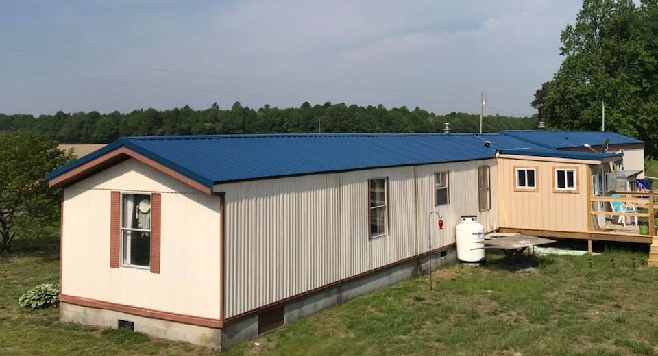 A mobile home with a blue roof is sitting in the middle of a grassy field.