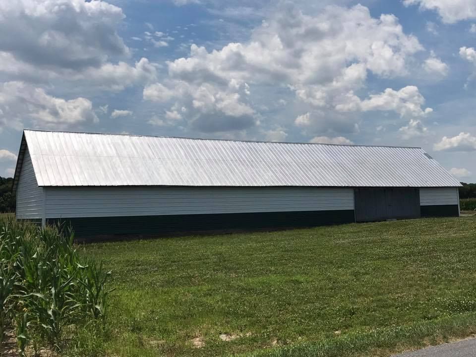 A large white barn is sitting in the middle of a grassy field.