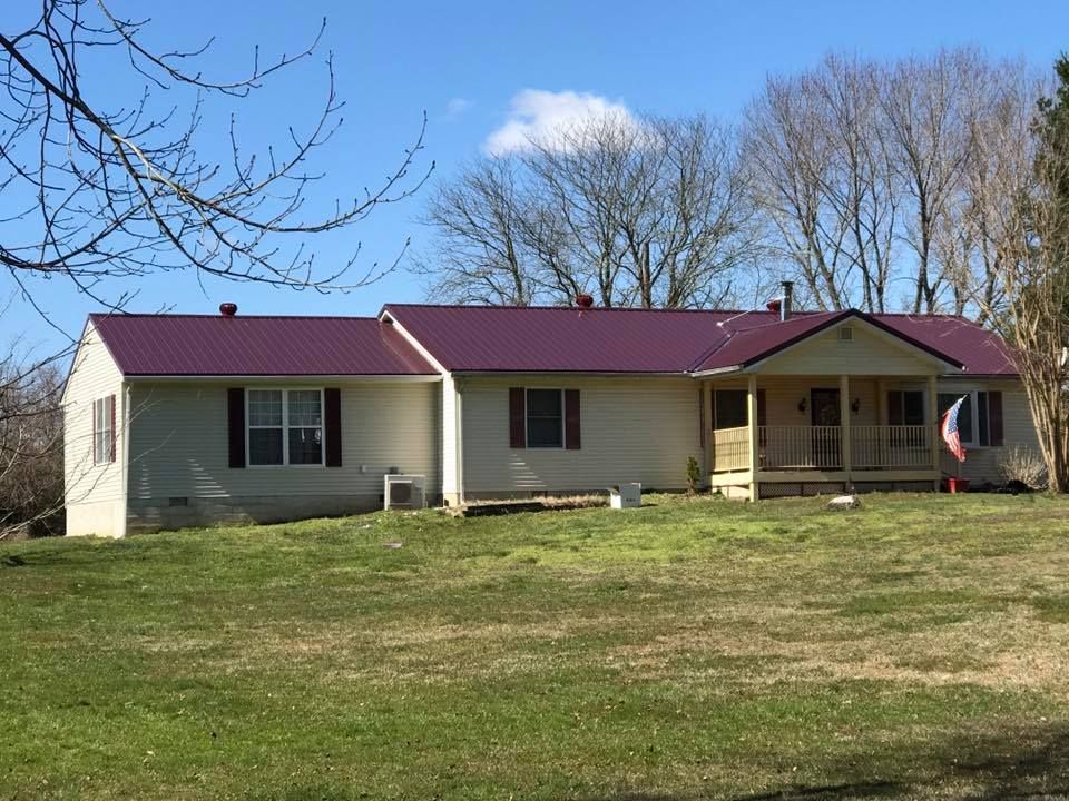 A white house with a red roof is sitting on top of a lush green field.