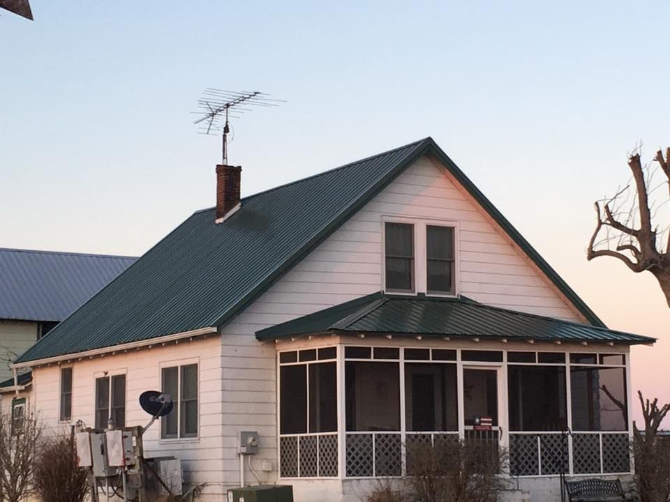 A white house with a green roof and a screened in porch