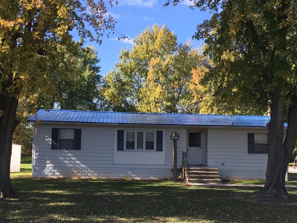 A white house with a blue roof is surrounded by trees