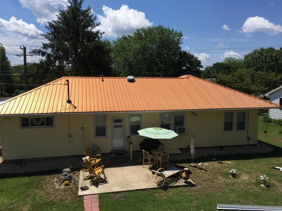 A yellow house with a copper roof and a patio with chairs and umbrellas.