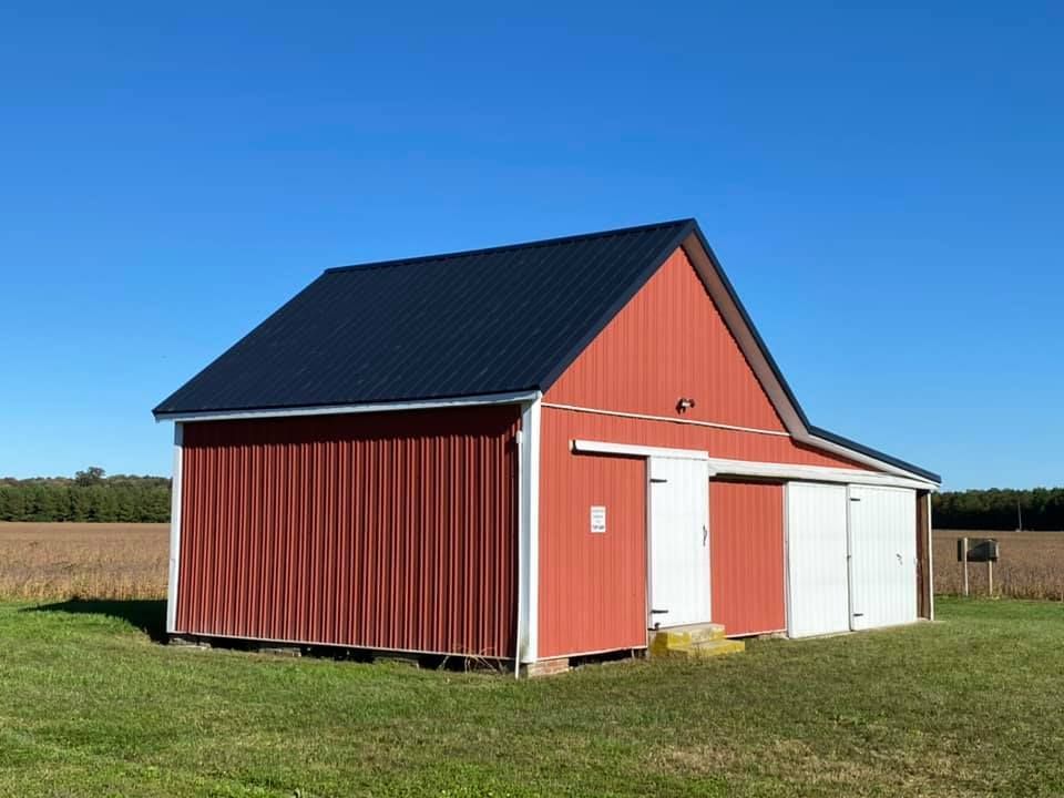 A red barn with a black roof sits in a grassy field