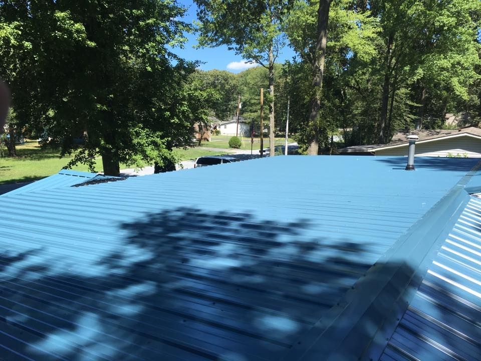 A blue roof of a house with trees in the background.
