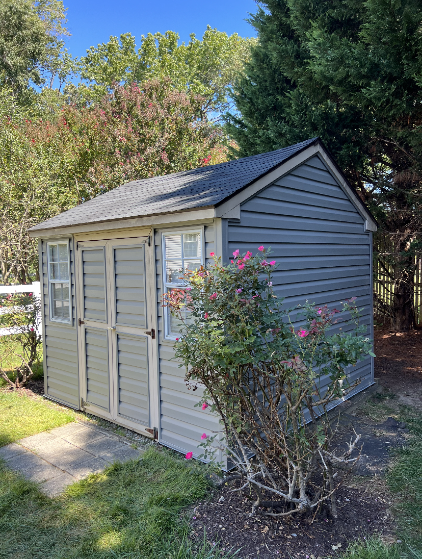 A gray shed with flowers in front of it in a yard.