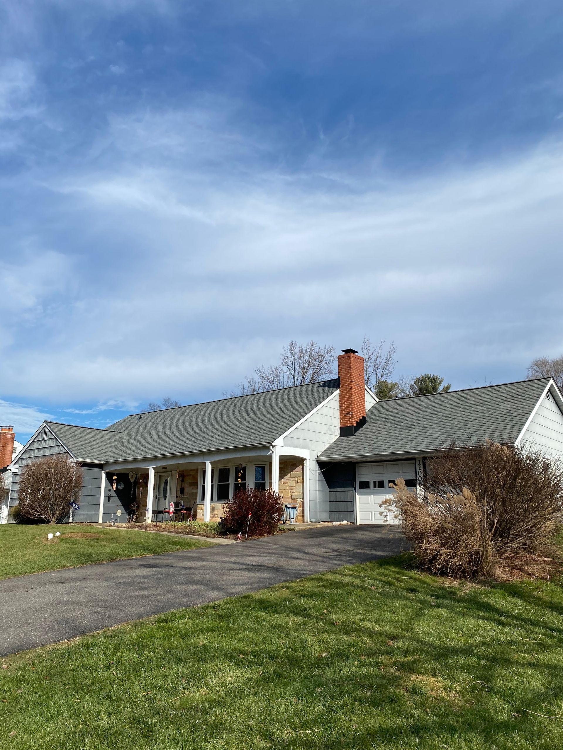 A white house with a gray roof is sitting on top of a lush green field.