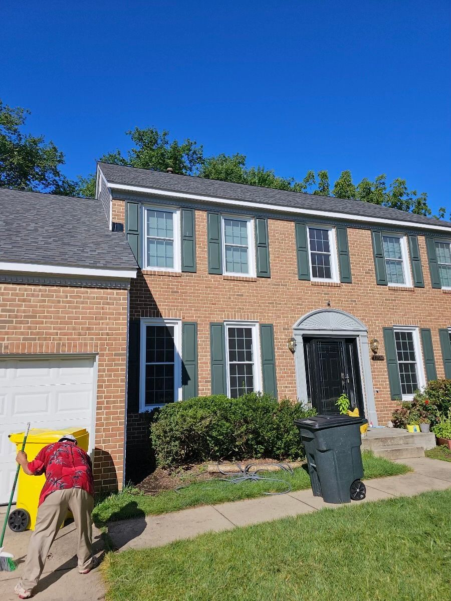 A man is standing in front of a brick house with green shutters.