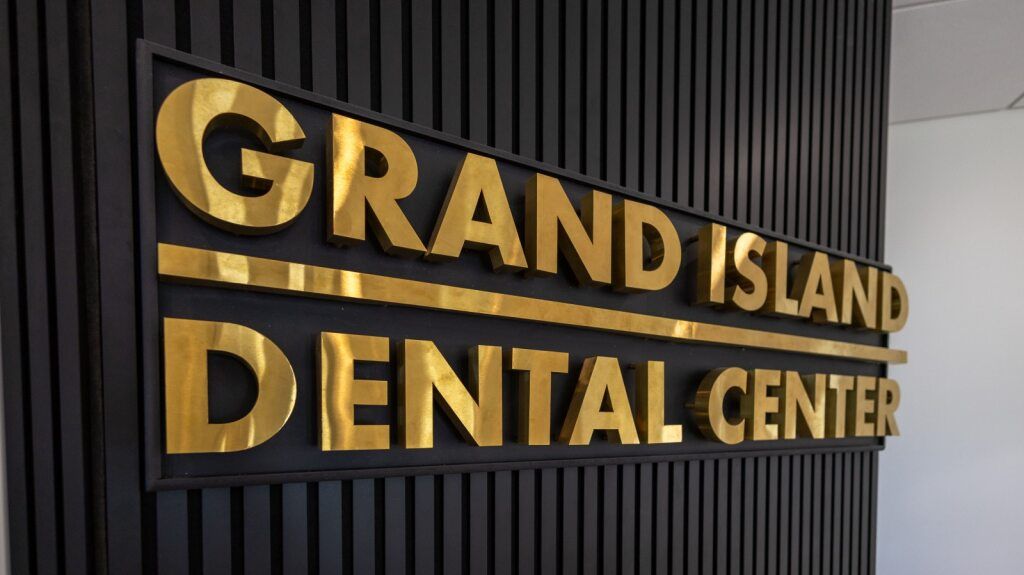 Gold lettering of Grand Island Dental Center on a black wall.