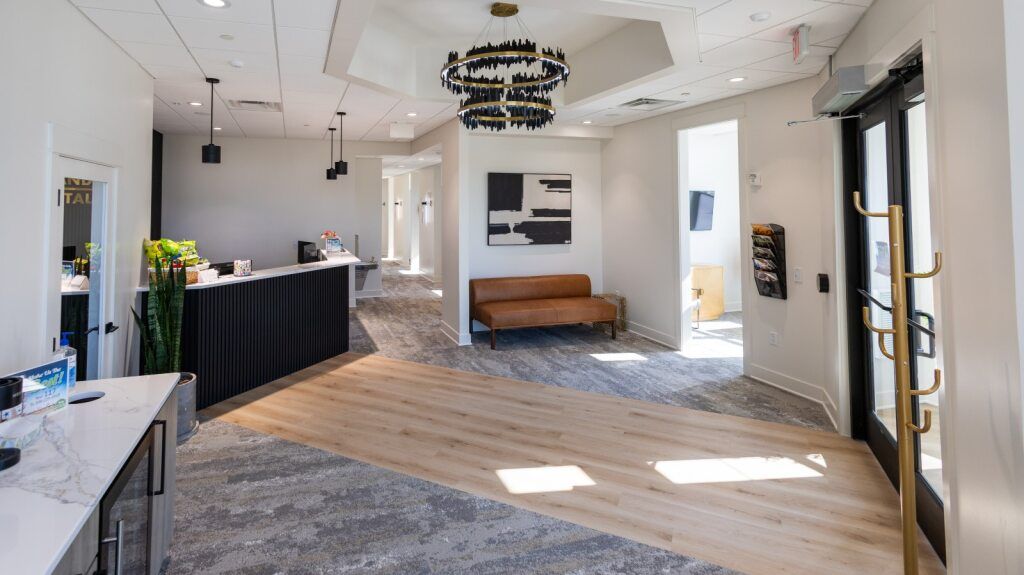 Bright reception area with a black and white front desk, tan leather sofa, and a modern chandelier.