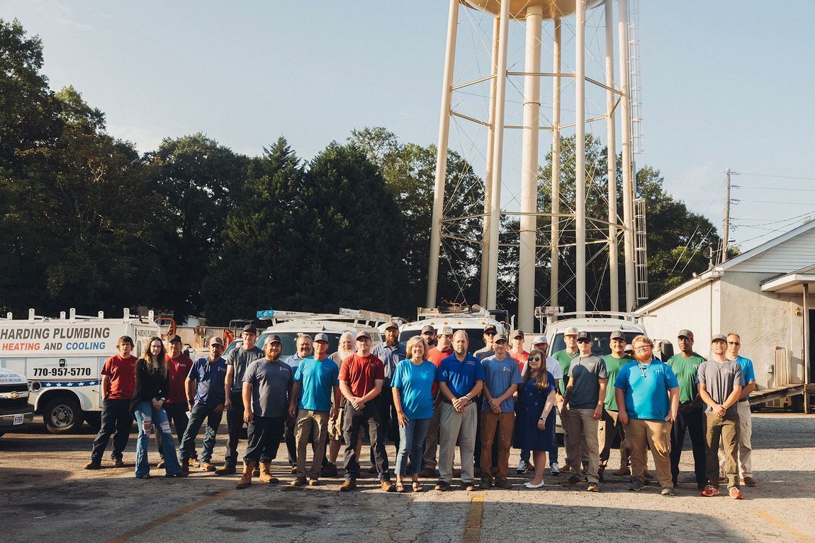 Group of people standing in front of utility trucks and a water tower. Most wear blue shirts.
