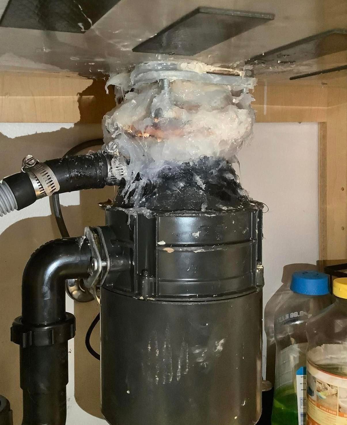Garbage disposal with white substance leaking from the top. Underneath a kitchen sink with attached plumbing.