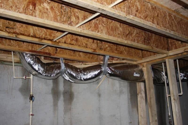 Silver ductwork suspended from wooden ceiling joists in a basement setting.