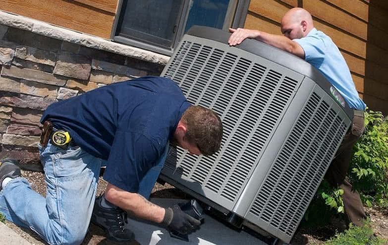 Two men installing an air conditioning unit near a building's exterior.