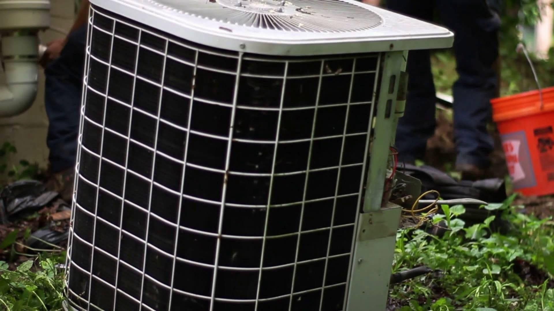 An outdoor air conditioning unit with black fins and a protective wire cage.