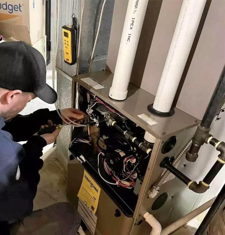 Person working on a furnace in a basement, using tools to adjust wiring.