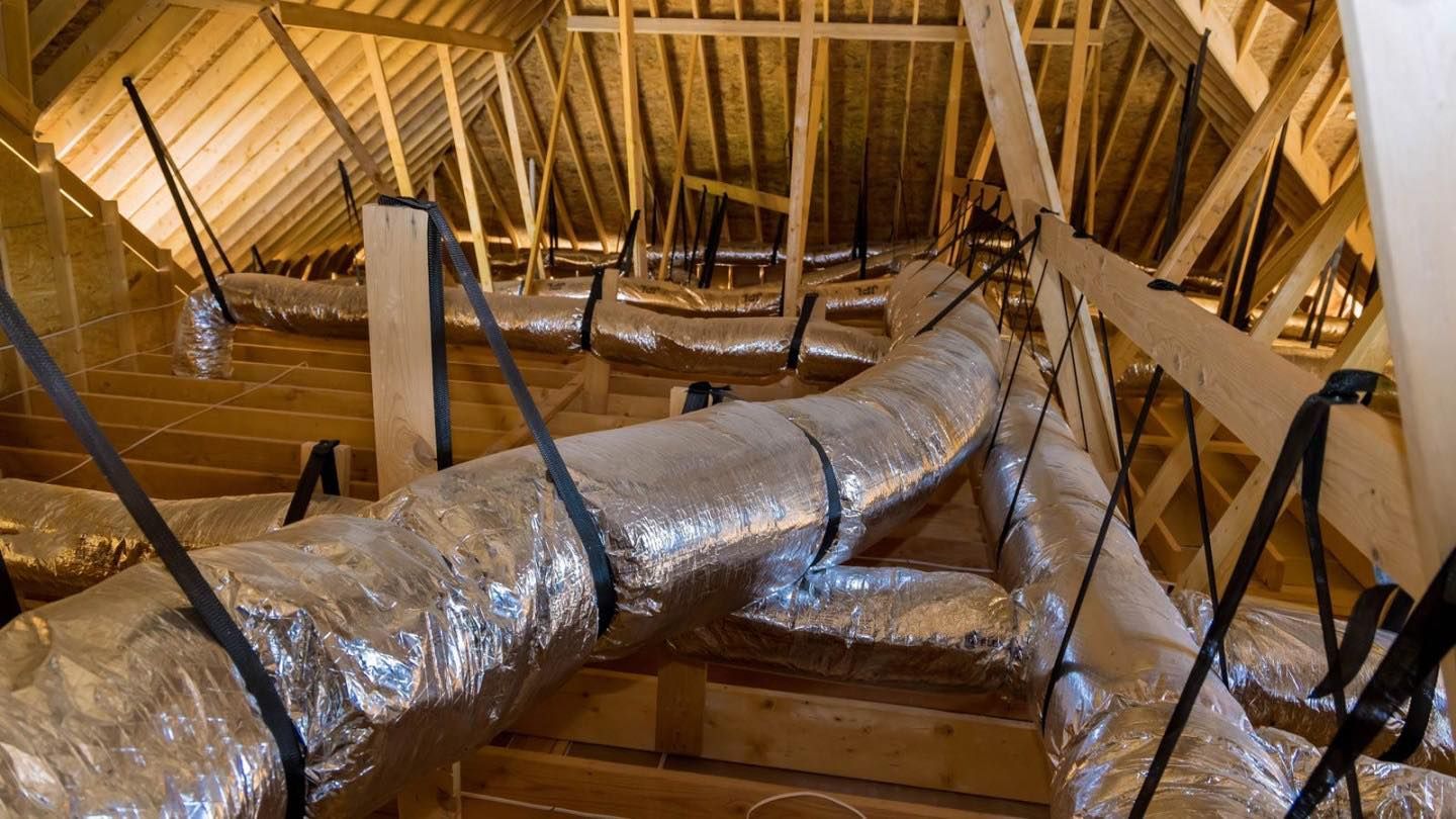 Attic with wooden beams and silver insulated air ducts secured with black straps.