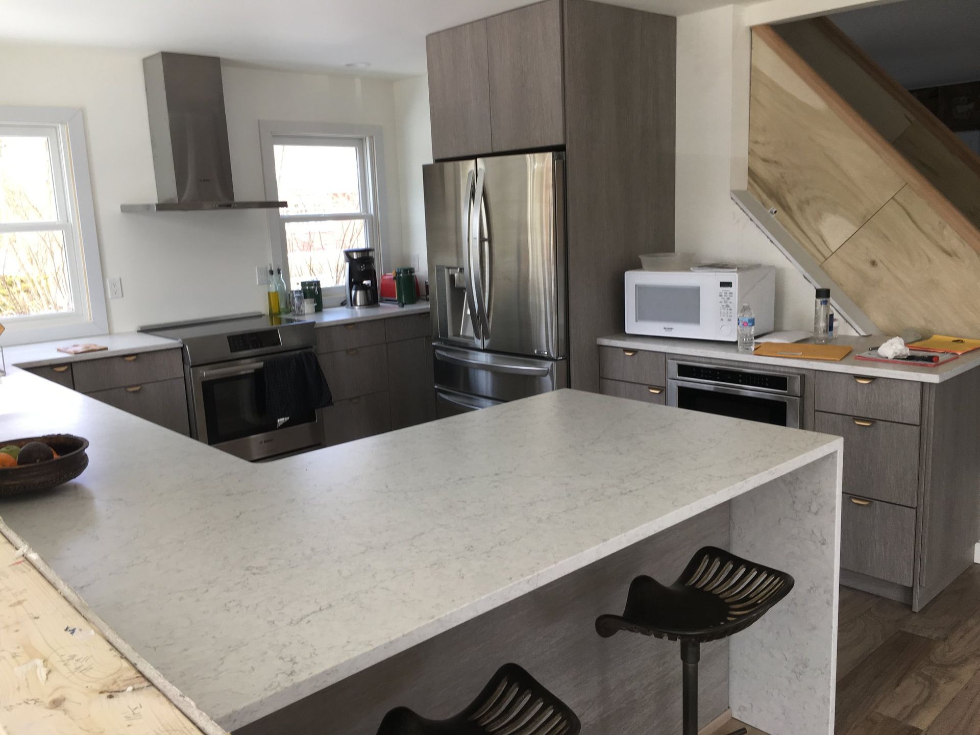 Modern kitchen with light countertops, gray cabinets, stainless steel appliances, and a breakfast bar with stools.