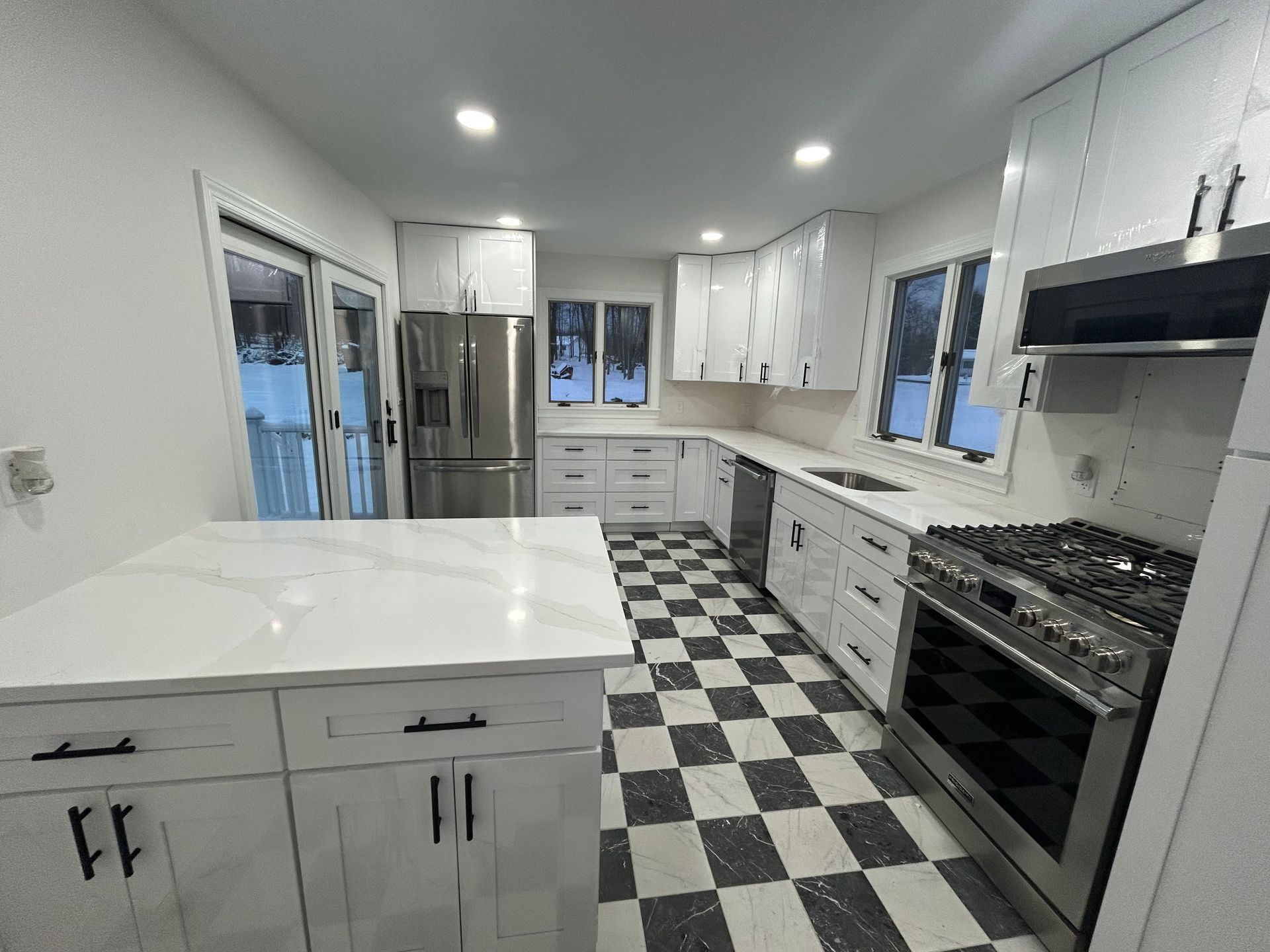 Modern white kitchen with stainless steel appliances, marble countertops, and checkered floor.