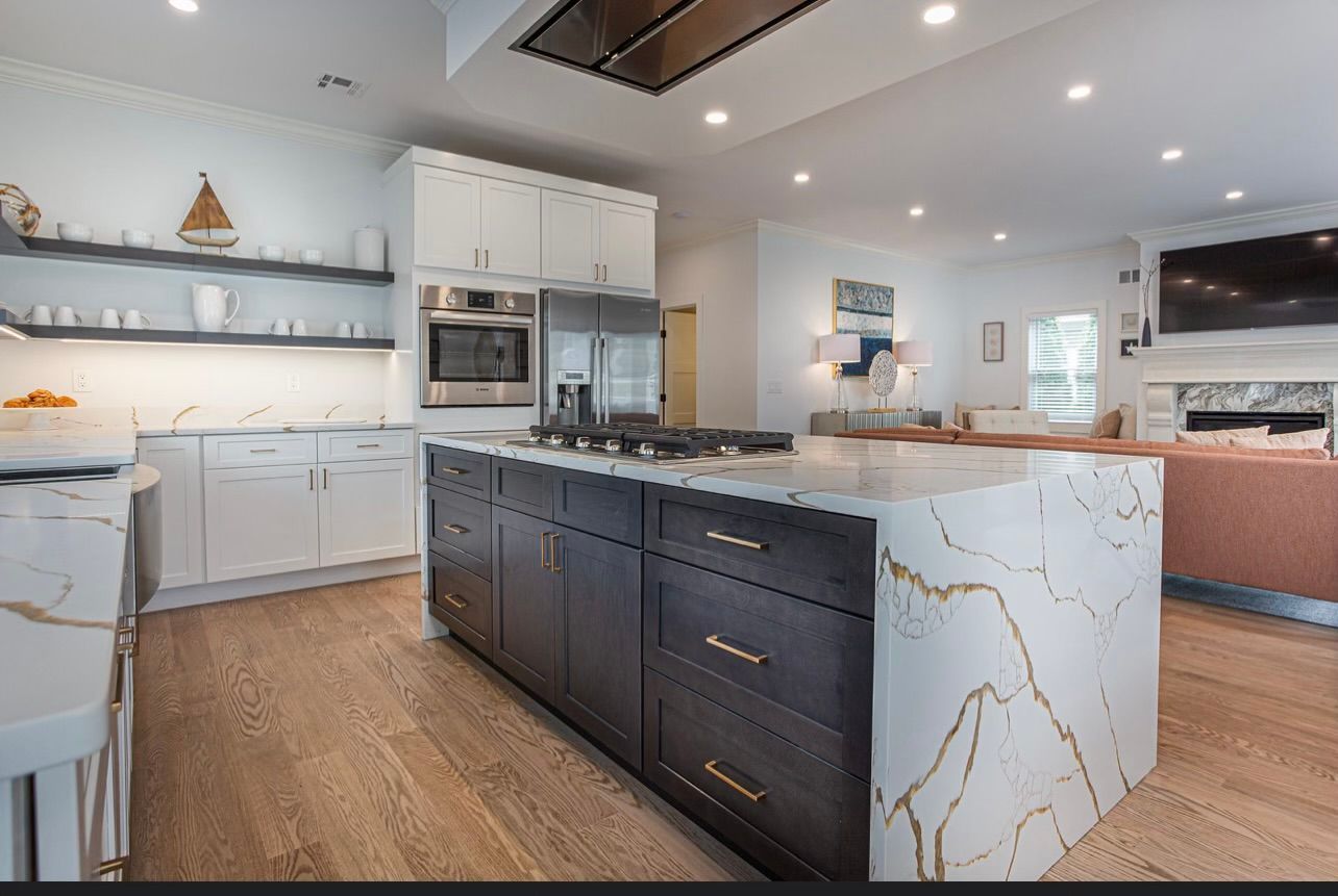 Modern kitchen with dark island and light countertops, open to living room with fireplace and TV.