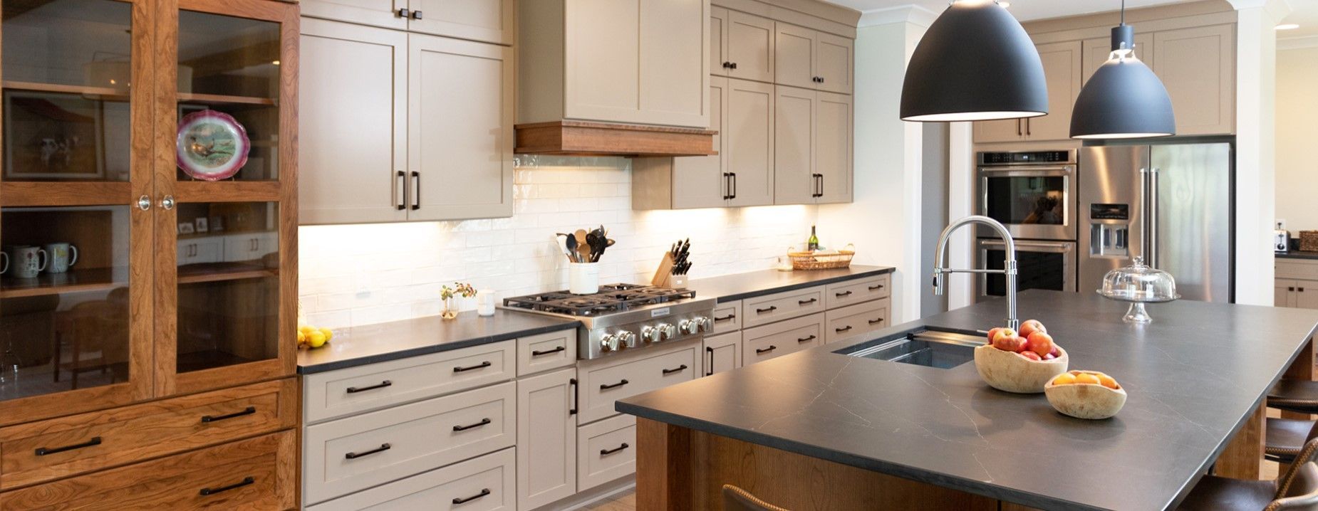 Modern kitchen with light cabinets, dark countertops, and an island. Two pendant lights hang above the island.