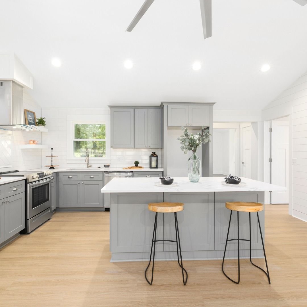 Modern kitchen with gray cabinets, white countertops, island with stools, and light wood floors.